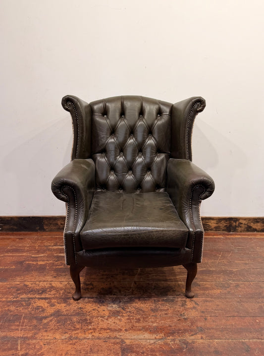 Stylish wingback armchair in dark green leather with fabric back