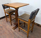 Tall Square Poseur Table with Two Patterned Bar Stools and Light Wood Finish